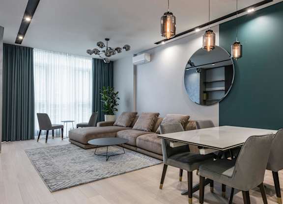 A modern living room with a grey sofa, a round mirror, and a glass table.
