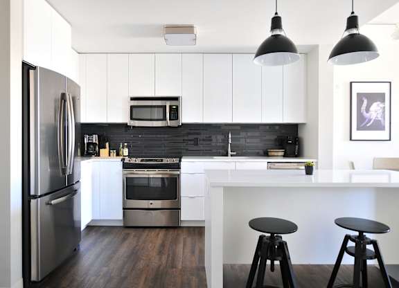 A modern kitchen with a refrigerator, microwave, oven, and bar stools.
