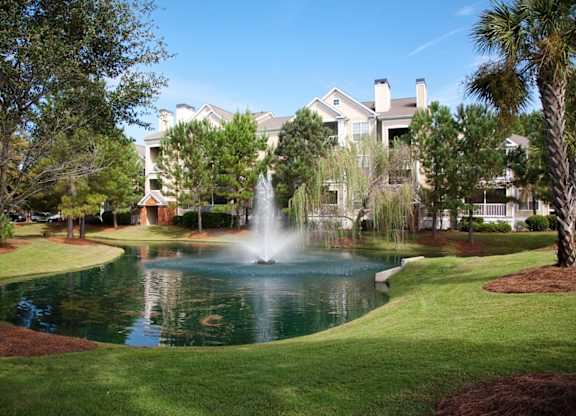 A fountain in the middle of a pond in front of a building.