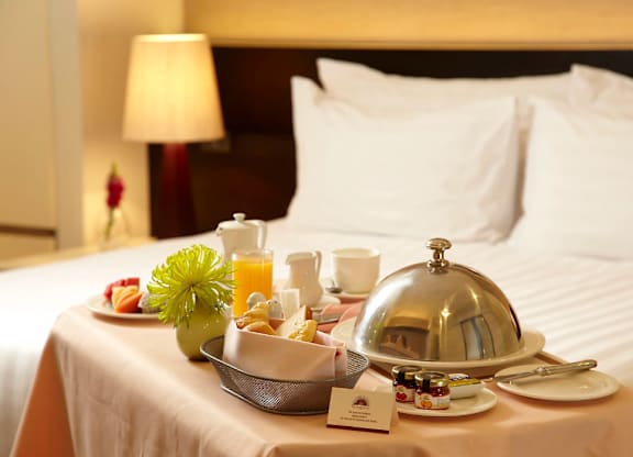 A tray of food is set on a bed with a silver bell on it.