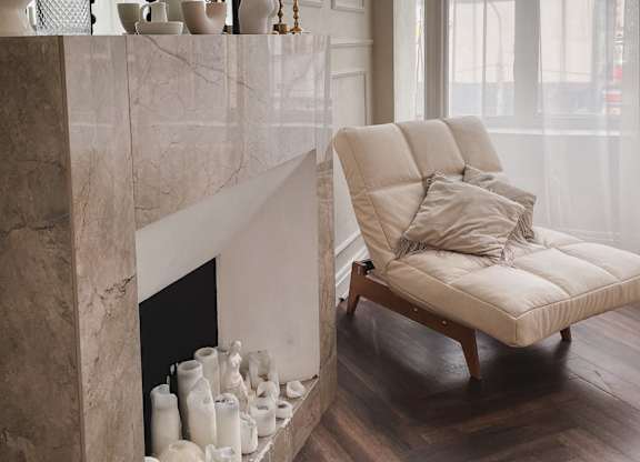 A white chair with a cushion is placed in front of a marble fireplace.