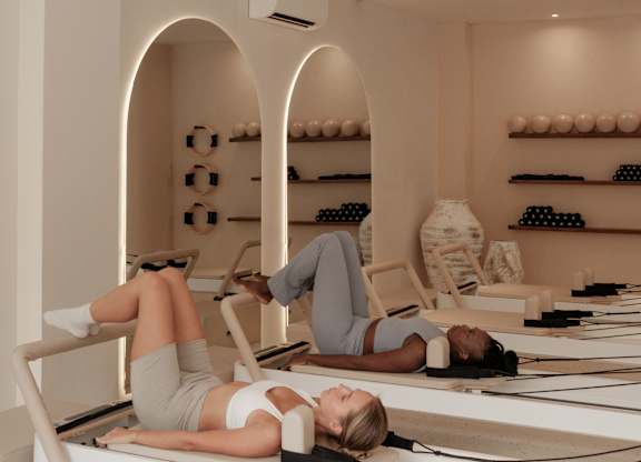 Two women are lying on reformers in a pilates studio.