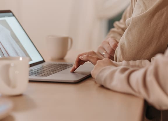 A person is typing on a laptop with a cup of coffee on the table.