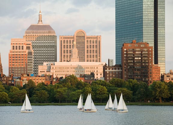 Three sailboats are sailing on a body of water in front of a city skyline.