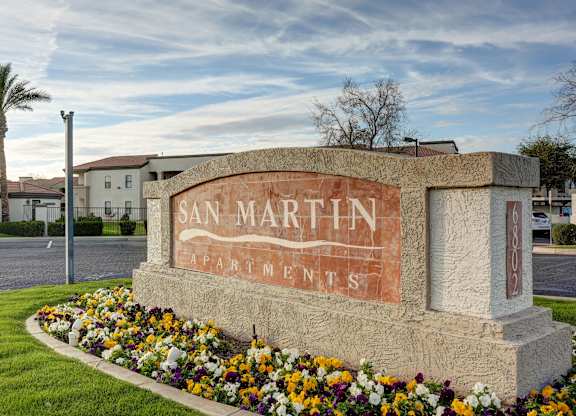 A sign for San Martin Apartments is surrounded by flowers.