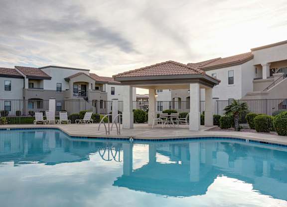 A swimming pool in front of a building with a gazebo.