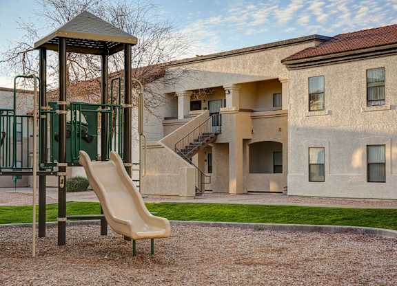 A playground with a slide and a chair in front of a building.
