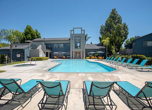 A pool surrounded by lawn chairs in front of a building at Autumn Oaks Apartments, Roseville, CA, 95678