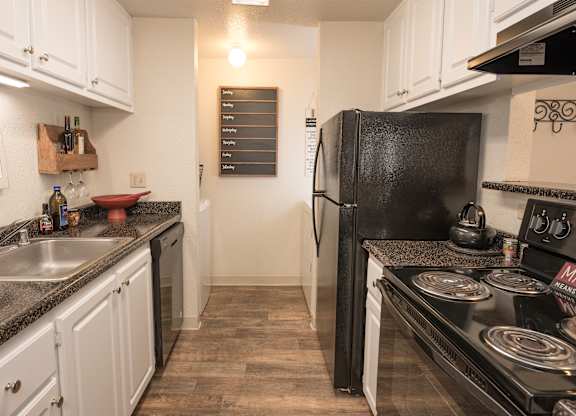 A kitchen with black appliances and white cabinets at Bishop's Court Apartments, California, 95670