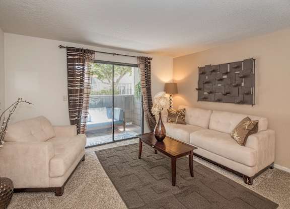 A living room with a white couch, a chair, a table, and a vase on the table at Bishop's Court Apartments, California, 95670
