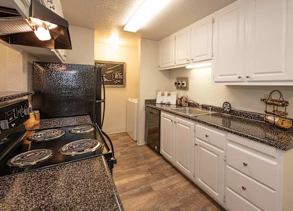 A kitchen with a black stove top oven and white cabinets at Bishop's Court Apartments, California, 95670