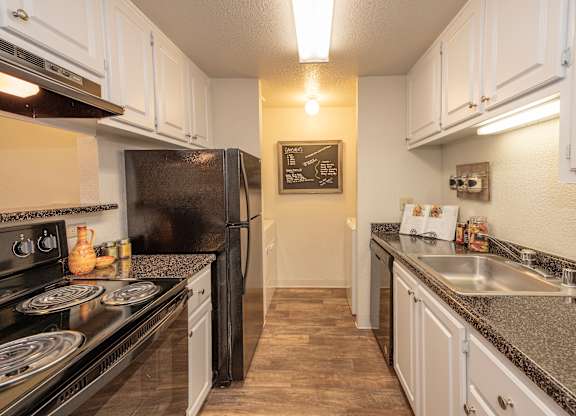 A kitchen with black appliances and white cabinets at Bishop's Court Apartments, California, 95670