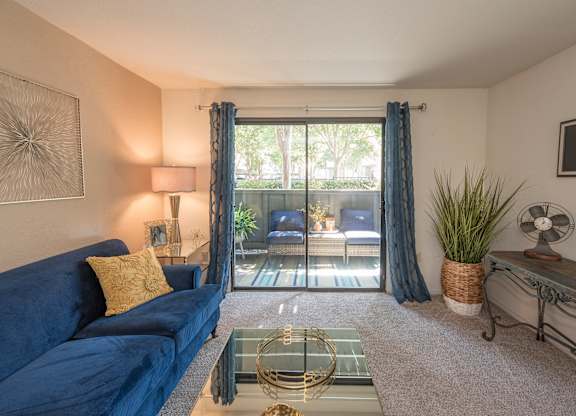 A living room with a blue couch and a glass coffee table at Bishop's Court Apartments, California, 95670