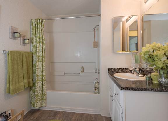Bathroom with a shower, green shower curtain, and green towels in a 2-bedroom, 1-bathroom apartment home at Bishop's Court Apartments in Rancho Cordova.