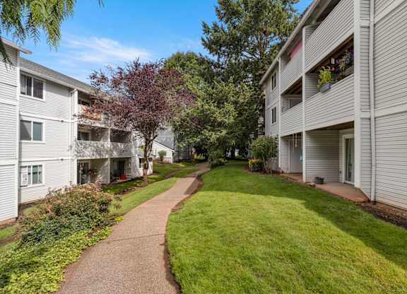 A pathway leads through a grassy area between two apartment buildings at Clackamas Trails Apartments, Oregon, 97222
