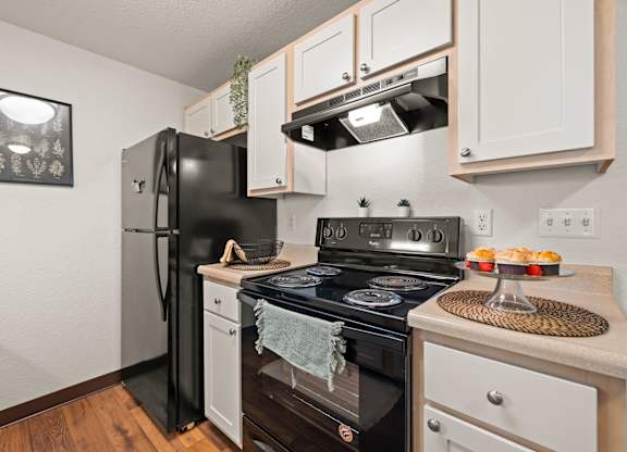 Model kitchen with black appliances, white cabinets, and vinyl plank flooring at Clackamas Trails Apartments, Oregon, 97222