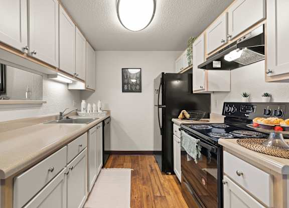 Model kitchen with black appliances, white cabinets, stainless steel sink and vinyl plank flooring at Clackamas Trails Apartments, Oregon, 97222