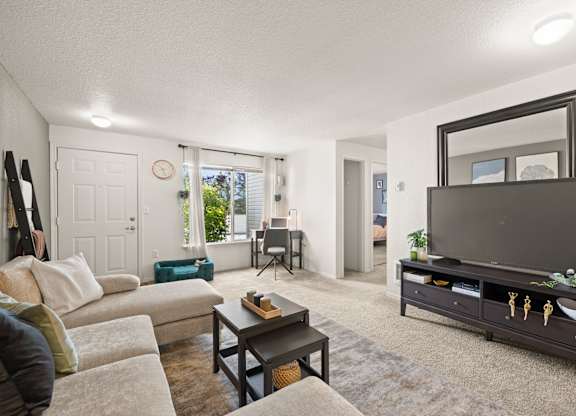 A living room with a couch, a coffee table, flat screen TV, and a large mirror at Clackamas Trails Apartments, Oregon, 97222