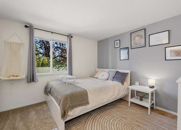 A bedroom with a bed, nightstand, and pictures on the wall at Clackamas Trails Apartments, Oregon, 97222