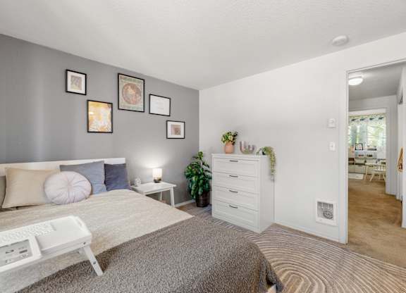 A bedroom with a bed, nightstand, and a wall with pictures at Clackamas Trails Apartments, Oregon, 97222
