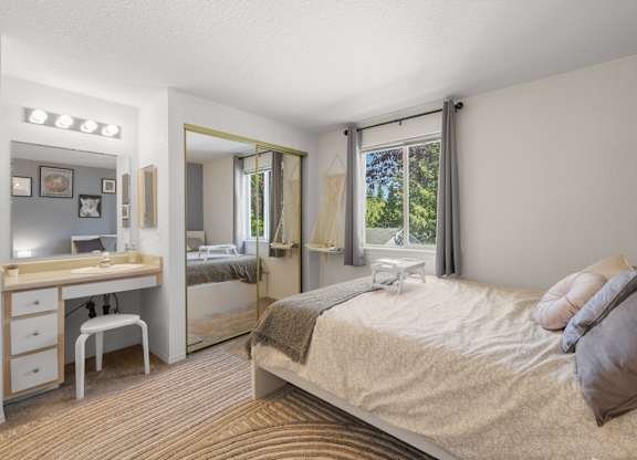 A bedroom with a bed, vanity, and chair at Clackamas Trails Apartments, Oregon, 97222