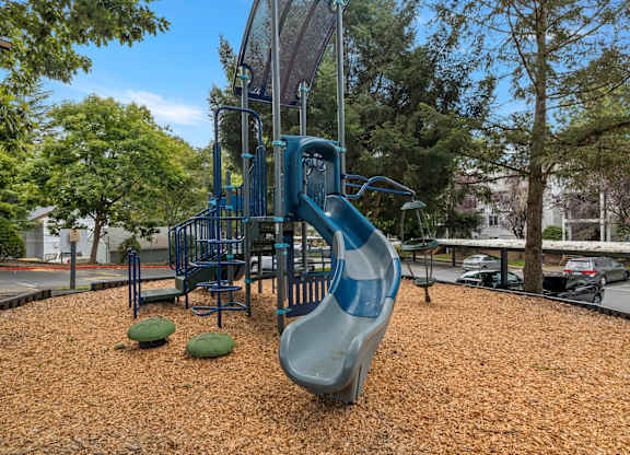 A playground with a blue slide and brown mulch at Clackamas Trails Apartments, Oregon, 97222