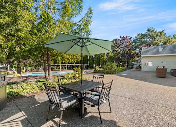 A table with two chairs and an umbrella is in the foreground of a pool at Clackamas Trails Apartments, Oregon, 97222
