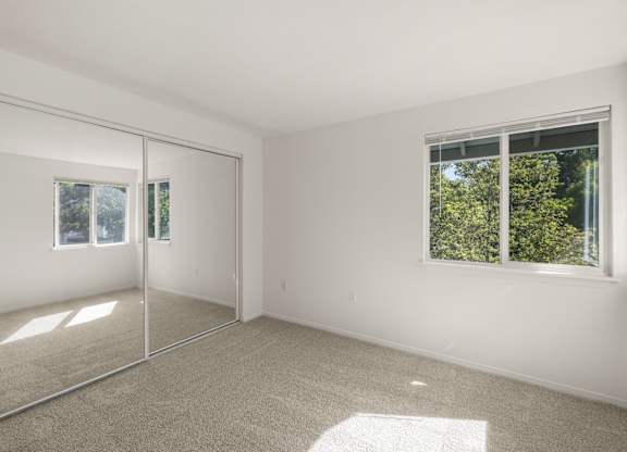 A room with a carpeted floor and a window showing trees outside at Clackamas Trails Apartments, Oregon, 97222
