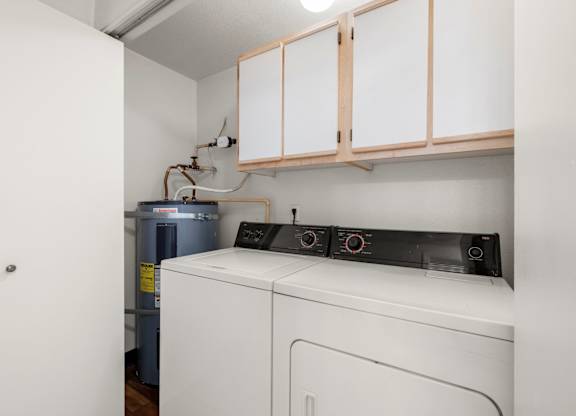 A white washing machine sits under a cabinet in a small room at Clackamas Trails Apartments, Oregon, 97222