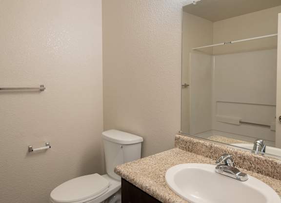 A bathroom with a toilet, sink, mirror, and towel bar at Pepperwood Apartments, California, 95661