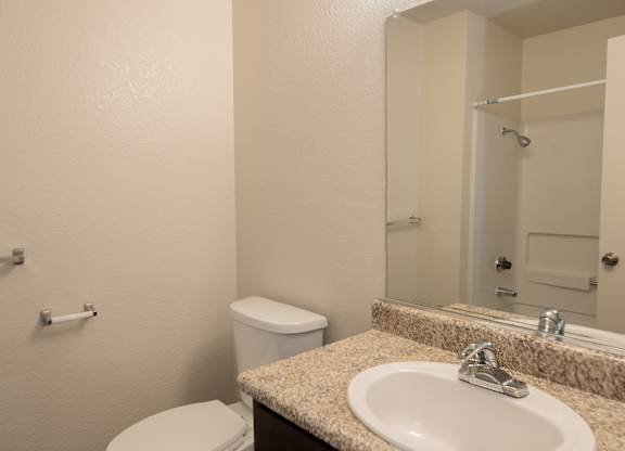 A bathroom with a toilet, sink, and mirror at Pepperwood Apartments, California, 95661