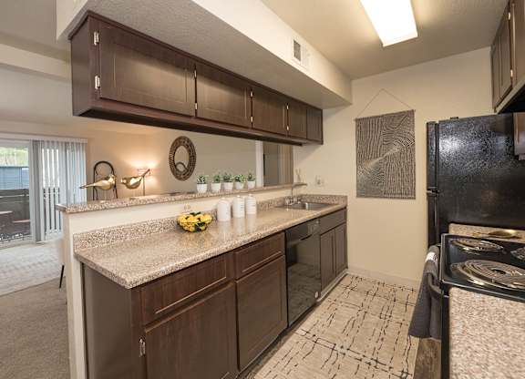 Model kitchen with brown cabinets and a black refrigerator at Pheasant Pointe Apartments, California, 95833