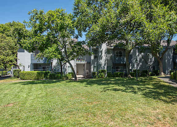 A grassy area in front of a building with trees at Rocklin Gold Apartments, California, 95677