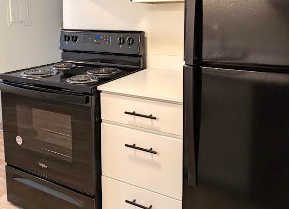A black refrigerator stands next to a black stove in a kitchen at Rolling Hills Apartments, Tualatin, 97062