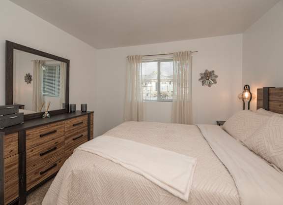 A bedroom with a large bed, a wooden dresser, and a window with curtains at Sierra Glen Apartments, California, 95621