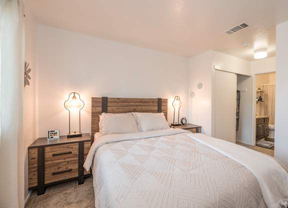 A bedroom with a large bed and two lamps on either side of the bed  at Sierra Glen Apartments, California, 95621