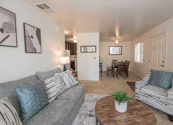 A living room with a grey couch, a wooden coffee table, and a striped armchair at Sierra Glen Apartments, Citrus Heights, California