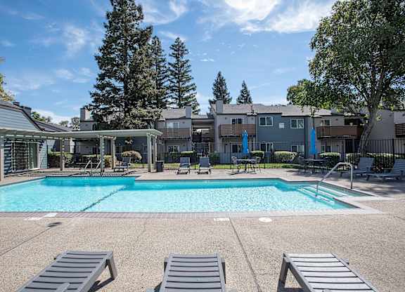 A large swimming pool surrounded by lounge chairs and trees at Sierra Glen Apartments, California, 95621