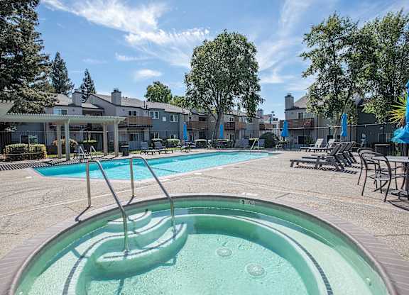 A hot tub sits in the middle of a pool area with a building in the background at Sierra Glen Apartments, California, 95621