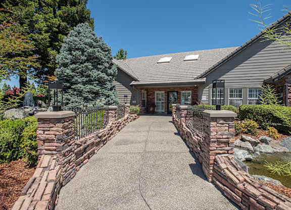 A clubhouse with a grey roof and a grey stone wall in front at Sunset Summit, Rocklin, CA, 95765