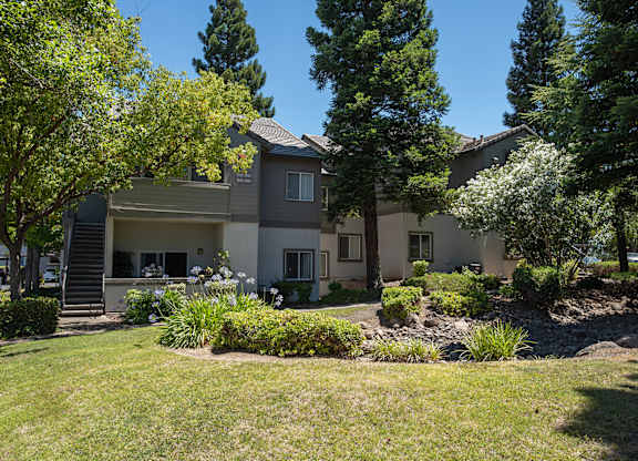 An apartment building with a well-maintained lawn and trees in the background at Sunset Summit, Rocklin, CA, 95765