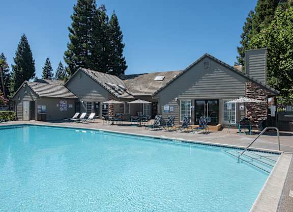 A large swimming pool in front of a clubhouse with a patio and lounge chairs at Sunset Summit, Rocklin, CA, 95765