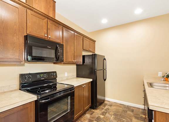 A kitchen with black appliances and wooden cabinets at The Landing Apartments and Townhomes, Oregon, 97045