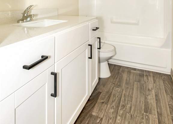A white bathroom with vinyl wood grain flooring and a white bathtub at Todd Village Apartments, Oregon, 97062