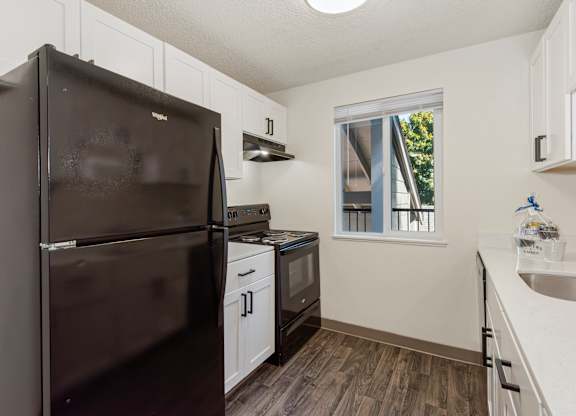 A black refrigerator is in a kitchen with white cabinets at Todd Village Apartments, Oregon, 97062