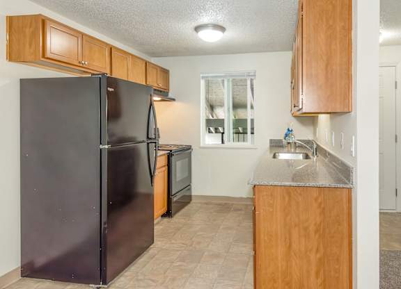 A kitchen with a black refrigerator and wooden cabinets at Todd Village Apartments, Oregon, 97062