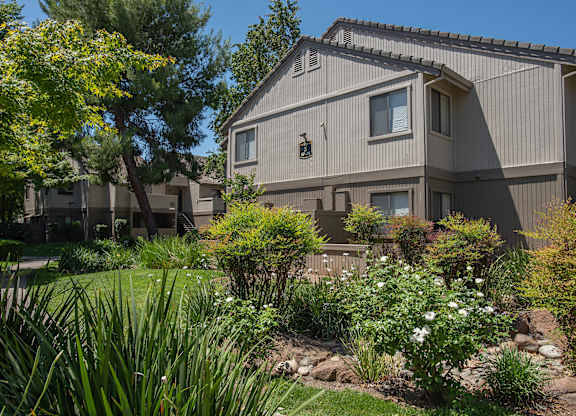An apartment building with a grey exterior and a garden in front at Zinfandel Village Apartments, California, 95670