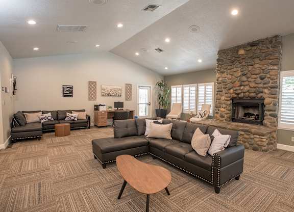 A clubhouse lounge with a stone fireplace and grey couches at Zinfandel Village Apartments, California, 95670