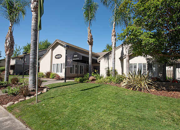A white clubhouse building with a black awning is surrounded by greenery at Zinfandel Village Apartments, California, 95670