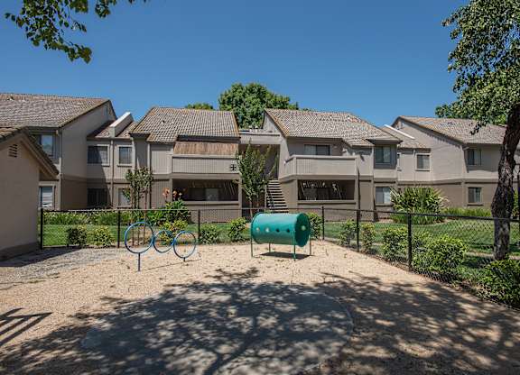A dog park with a green barrel and two blue rings in front of apartment buildings at Zinfandel Village Apartments, California, 95670